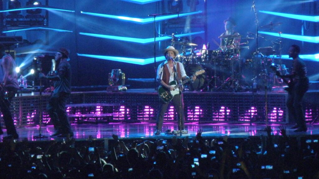 A imagem mostra o cantor Bruno Mars em uma apresentação ao vivo.